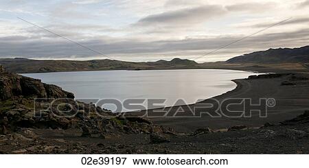 Serene lake with volcanic black sand and rocky hill View Large Photo Image Stock Photo - Serene lake with volcanic black sand and rocky hill. Fotosearch