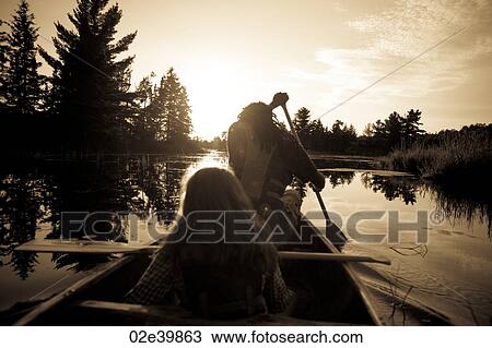 Stock Image - Sillhouette of people rowing a canoe at Lake of the Woods, Ontario. Fotosearch