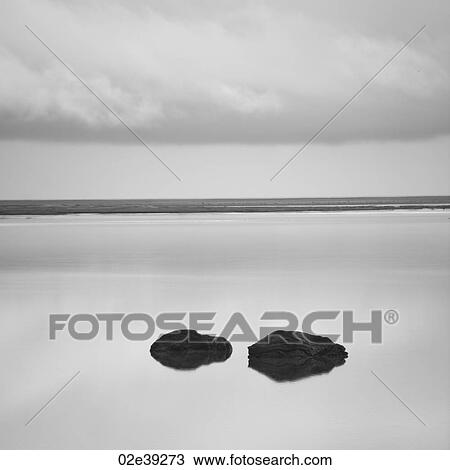Stock Image - Solitary rocks in calm lake under cloudy sky near shore. Fotosearch