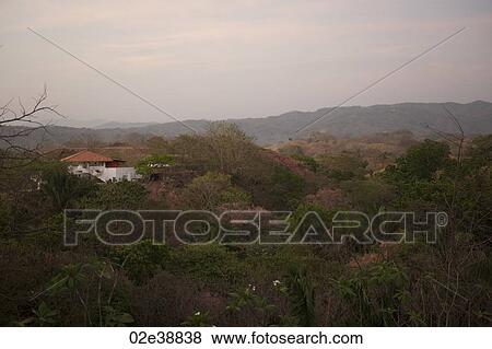 Sun fading over a white house with an orange roof in the rolling hills above the treetops of Costa Rica View Large Photo Image Stock Photo - Sun fading over a white house with an orange roof in the rolling hills above the treetops of Costa Rica. Fotosearch