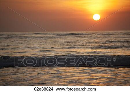 Sun setting over the calm ocean with an orange glow View Large Photo Image Picture - Sun setting over the calm ocean with an orange glow. Fotosearch