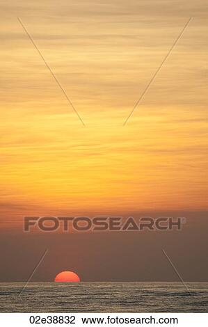 Sun setting over the calm ocean with an orange glow View Large Photo Image Stock Image - Sun setting over the calm ocean with an orange glow. Fotosearch