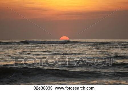 Sun setting over the calm ocean with an orange glow View Large Photo Image Stock Image - Sun setting over the calm ocean with an orange glow. Fotosearch
