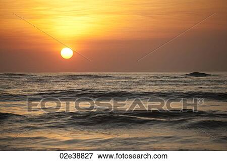 Sun setting over the calm ocean with an orange glow View Large Photo Image Stock Photo - Sun setting over the calm ocean with an orange glow. Fotosearch