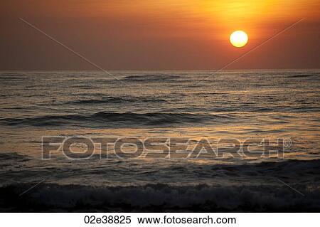 Sun setting over the calm ocean with an orange glow View Large Photo Image Stock Photography - Sun setting over the calm ocean with an orange glow. Fotosearch