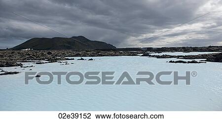 Stock Image - Volcanic geothermal lagoon, rugged landscape, stormy sky. Fotosearch
