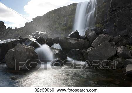 Waterfall cascading onto boulders into a river View Large Photo Image Stock Image - Waterfall cascading onto boulders into a river. Fotosearch