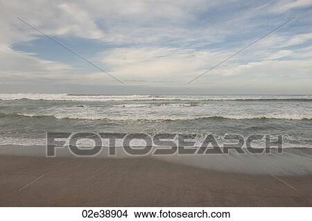 Picture - Waves breaking on the beach under a cloudy blue sky. Fotosearch