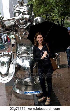 Stock Image - Woman standing beside a statue, Shanghai, China. Fotosearch