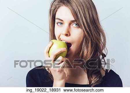 Beautiful young woman bites a green apple on a gray background View Large Photo Image Stock Image - Beautiful young woman bites a green apple on a gray background. Fotosearch