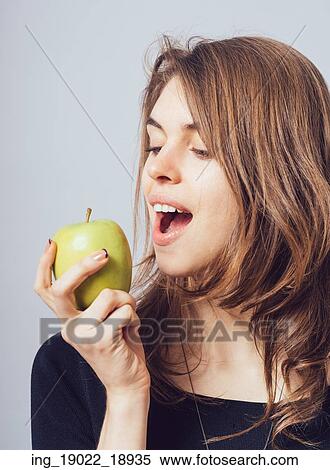 Beautiful young woman bites a green apple on a gray background View Large Photo Image Stock Photography - Beautiful young woman bites a green apple on a gray background. Fotosearch