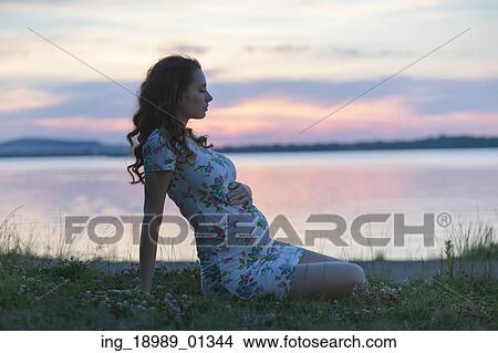Picture - Calm pregnant lady sitting on the lakeside. Fotosearch