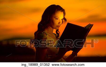 Stock Image - Charming woman reading interesting, shining book. Fotosearch