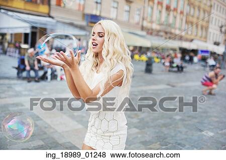 Stock Photo - Cheerful blond lady carrying huge soap bubble. Fotosearch