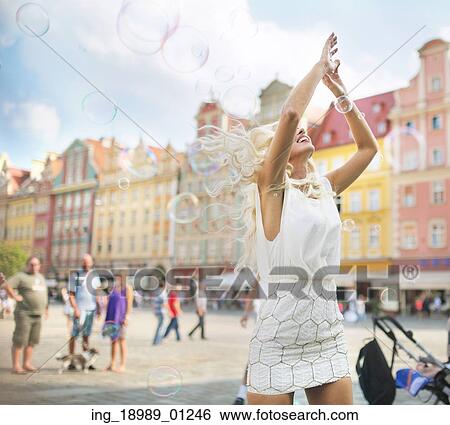 Stock Photograph - Delicate blond woman catching flying soap bubbles. Fotosearch