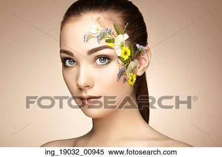 Stock Photography - Face of beautiful woman decorated with flowers. Perfect makeup. Beauty fashion. Eyelashes. Cosmetic Eyeshadow. Fotosearch