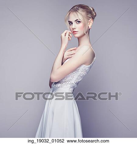 Stock Image - Fashion portrait of beautiful young woman with blond hair. Girl in white dress on white background. Fotosearch