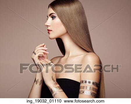 Stock Image - Fashion portrait of elegant woman with magnificent hair. Blonde girl. Perfect make-up. Girl in elegant dress. Flash tattoo gold. Fotosearch
