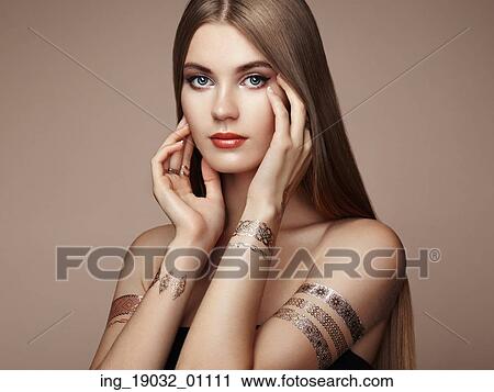 Stock Image - Fashion portrait of elegant woman with magnificent hair. Blonde girl. Perfect make-up. Girl in elegant dress. Flash tattoo gold. Fotosearch