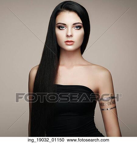 Stock Image - Fashion portrait of elegant woman with magnificent hair. Brunette girl. Perfect make-up. Girl in elegant dress. Flash tattoo gold. Fotosearch