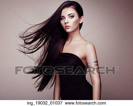 Stock Photo - Fashion portrait of elegant woman with magnificent hair. Brunette girl. Perfect make-up. Girl in elegant dress. Flash tattoo gold. Fotosearch