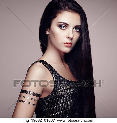 Stock Photo - Fashion portrait of elegant woman with magnificent hair. Brunette girl. Perfect make-up. Girl in elegant dress. Flash tattoo gold. Fotosearch
