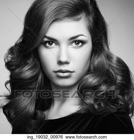 Stock Photograph - Fashion portrait of elegant woman with magnificent hair. Brunette girl. Perfect make-up. Girl in black dress. Curly hair. Fotosearch
