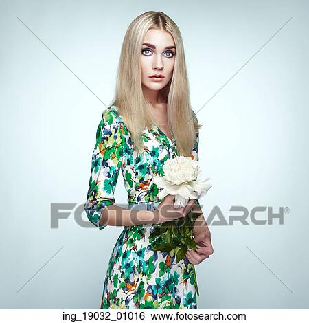 Stock Photograph - Fashion portrait of elegant woman with summer flowers. Blonde girl. Perfect make-up. Hairstyle. Summer dress. Peonies. Fotosearch