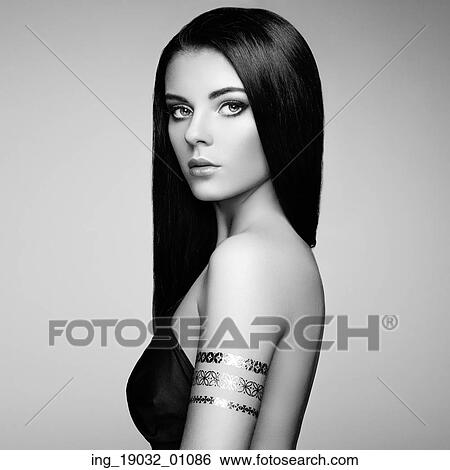 Stock Photograph - Fashion portrait of elegant woman with magnificent hair. Brunette girl. Perfect make-up. Girl in elegant dress. Flash tattoo gold. Black and white. Fotosearch