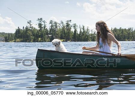 Stock Image - Girl rowing a canoe with a puppy, Lake of the Woods, Ontario, Canada. Fotosearch