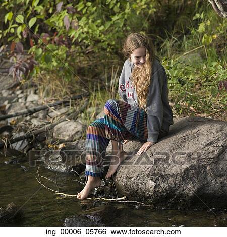 Stock Photograph - Girl sitting on rock at lakeside, Lake of the Woods, Ontario, Canada. Fotosearch