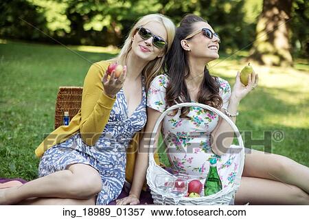 Stock Photo - Glad women eating tasty juicy fruit. Fotosearch