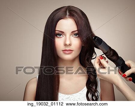 Stock Image - Hairdresser woman curls her hair. Portrait of young beautiful girl with luxurious hair. Fashion and beauty. Perfect make-up. Fotosearch