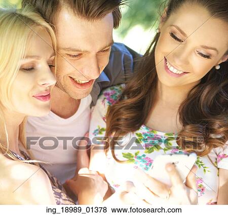 Stock Photo - Joyful friends testing new mobile phone. Fotosearch