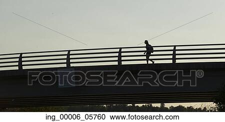 Stock Image - Low angle view of a woman walking on bridge, Kenora, Lake of the Woods, Ontario, Canada. Fotosearch