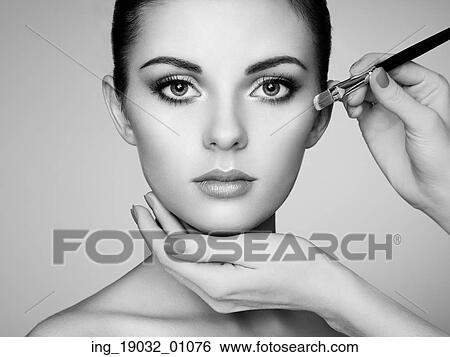 Stock Photograph - Makeup artist applies skintone. Beautiful woman face. Perfect makeup. Skincare foundation. Black and white. Fotosearch