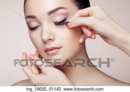 Stock Image - Makeup artist glues eyelashes. Beautiful woman face. Perfect makeup. Beauty fashion. Eyelashes. Cosmetic Eyeshadow. Fotosearch