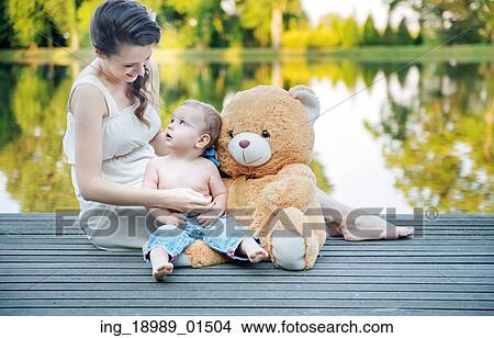 Picture - Mom looking at her baby playing teddy bear. Fotosearch