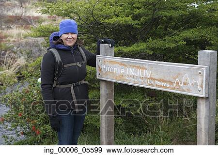 Stock Photo - Portrait of a woman standing near a signboard, Torres Del Paine National Park, Patagonia, Chile. Fotosearch