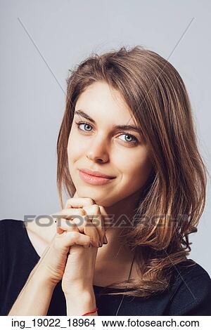 Picture - portrait of beautiful young brunette girl holding hand on chin isolated on gray background. Fotosearch