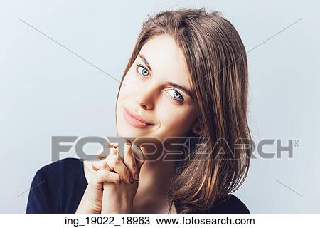 Stock Image - portrait of beautiful young brunette girl holding hand on chin isolated on gray background. Fotosearch