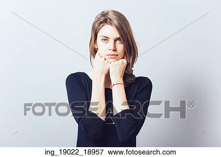 Stock Photo - portrait of beautiful young brunette girl holding hand on chin isolated on gray background. Fotosearch