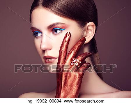 Picture - Portrait of beautiful young woman with art make-up. Bronze hand. Beauty fashion. Fotosearch