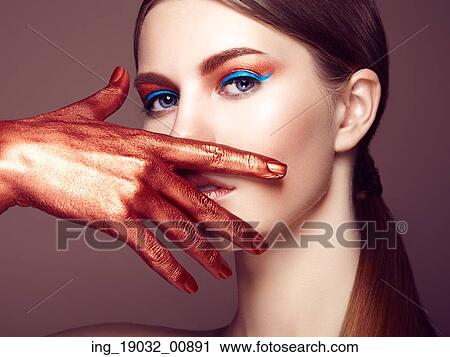 Stock Image - Portrait of beautiful young woman with art make-up. Bronze hand. Beauty fashion. Fotosearch