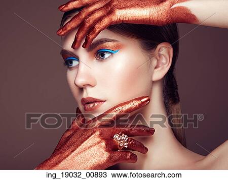 Stock Image - Portrait of beautiful young woman with art make-up. Bronze hand. Beauty fashion. Fotosearch