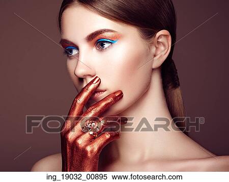 Stock Photography - Portrait of beautiful young woman with art make-up. Bronze hand. Beauty fashion. Fotosearch