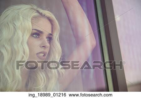 Stock Photograph - Portrait of the blond lady behind the window. Fotosearch