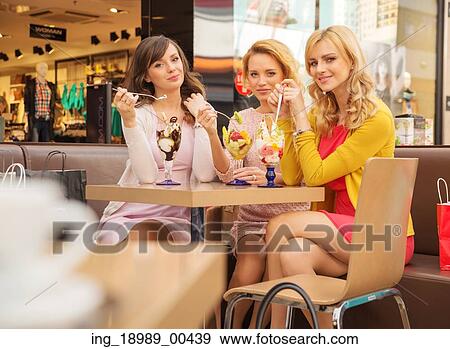 Stock Photo - Portrait of the young cherful girlfriends eating ice cream. Fotosearch