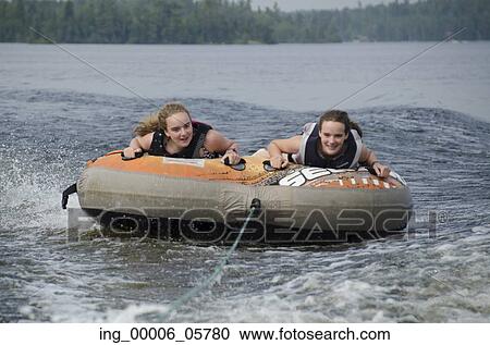 Stock Image - Portrait of two girls lying on an inflatable raft floating in a lake, Lake Of The Woods, Ontario, Canada. Fotosearch