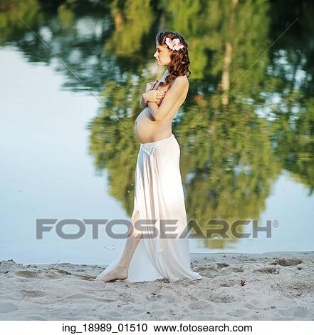 Stock Image - Pregnant woman walking on the beach. Fotosearch